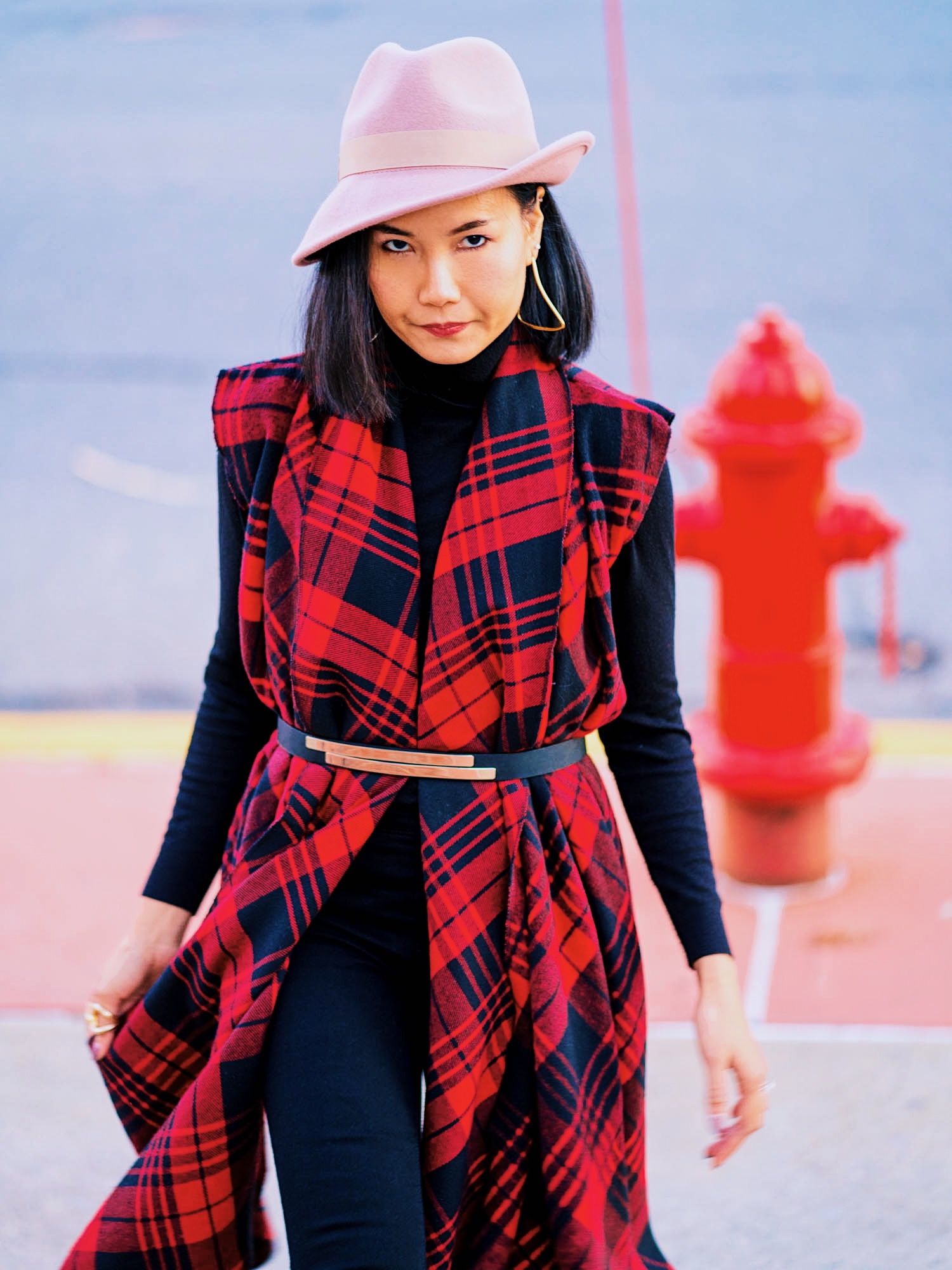 outfit detail shot for wearing all black outfit with a flannel vest, pink asymmetrical hat and jewelry